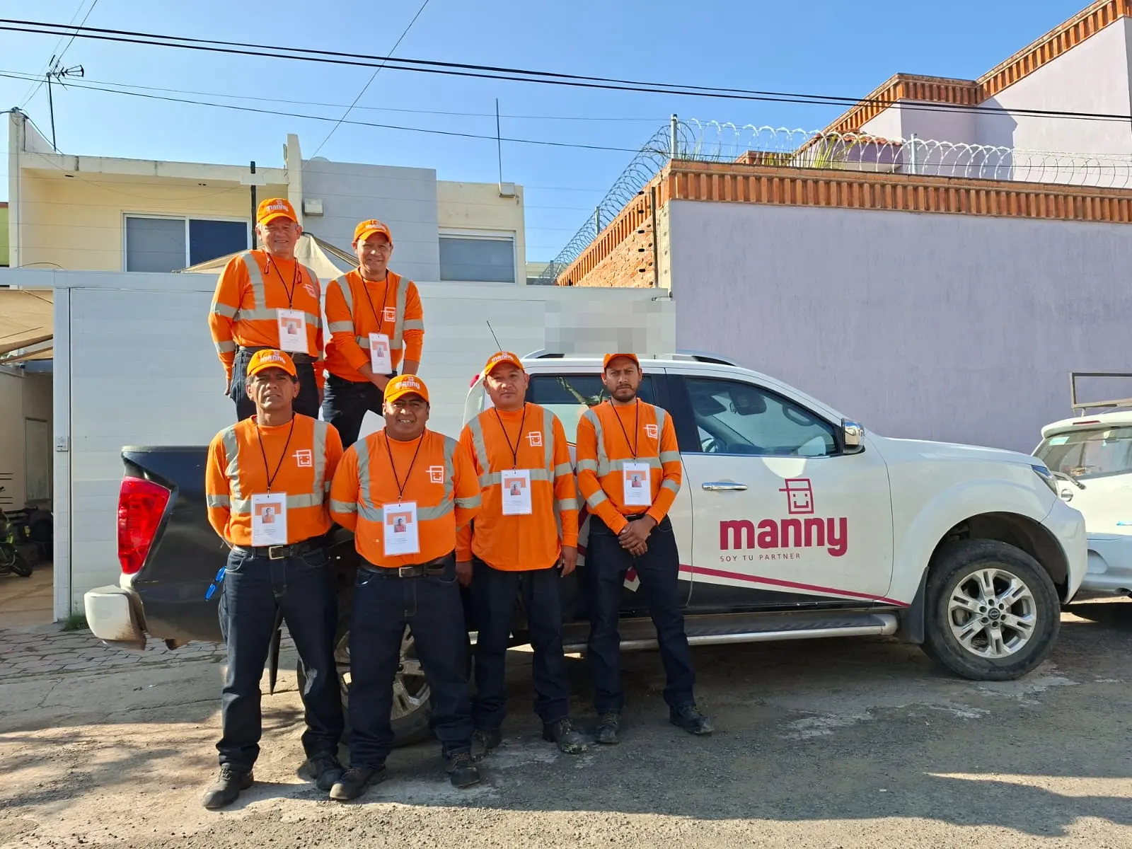 Seis integrantes del equipo de Manny, uniformados y con credencial a la vista, frente a una camioneta rotulada de la casa